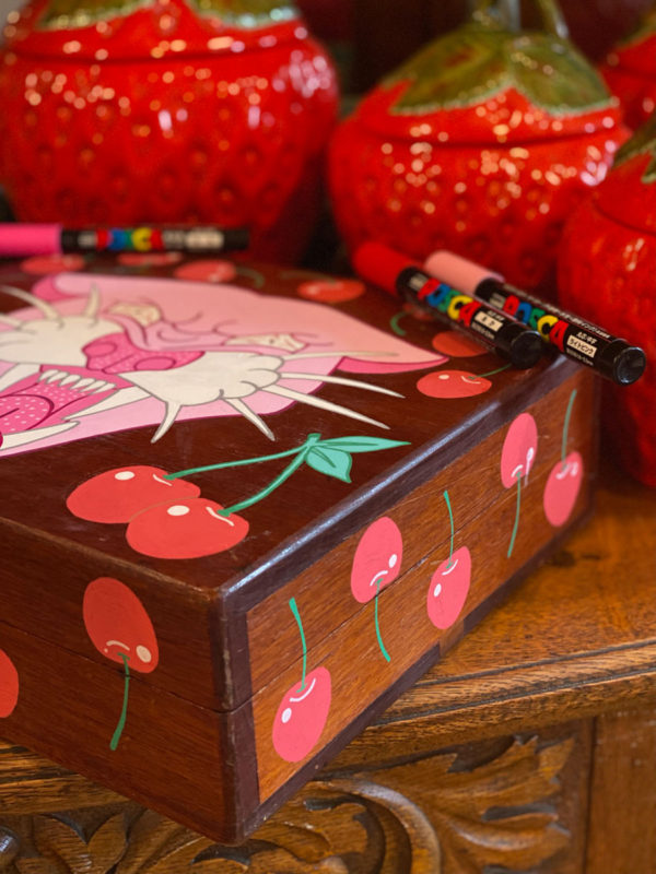 Close up photo of a hand painted wooden box with a pink panther and red cherries